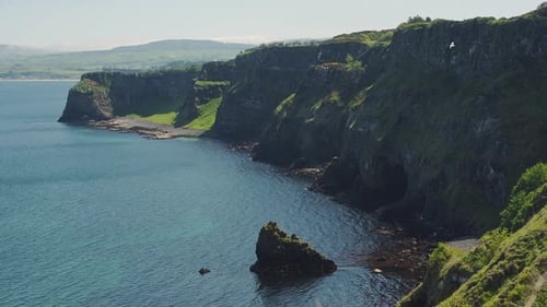 Lush Cliff Surrounded By Dark Blue Sea In Rathlin Island, Ireland With A Bird Flying On A Sunny Day