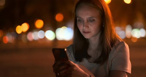 Young Girl in the Night City Writes Text Messages in a Smartphone