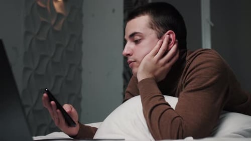 Young Adult Using Mobile Phone Lying in Bed