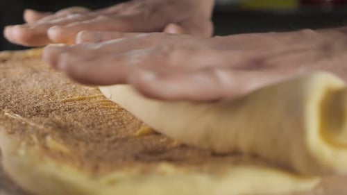 Baker Chef Rolls the Dough with Cinnamon Sugar and Butter Into a Roll on the Table