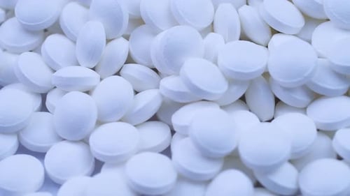 A Large Number of White Pills Lie Together and Rotate on a Table Close-up