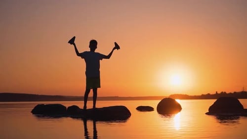 A happy child is playing with a paper airplane at sunset.