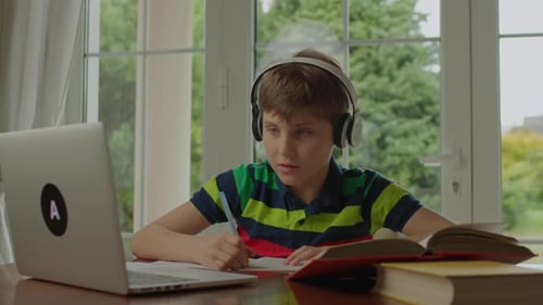 School Boy Learning Using Laptop Sitting at the Table By the Window