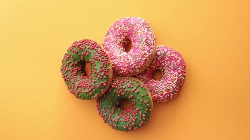 Komposition von oben mit einer Portion mehrfarbiger süßer Donuts, die einzeln auf gelbem Grund rotieren