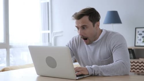 Man on Laptop Looks Worried at Table Indoors