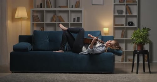 Young Woman Plays Guitar Lying on Couch at Home