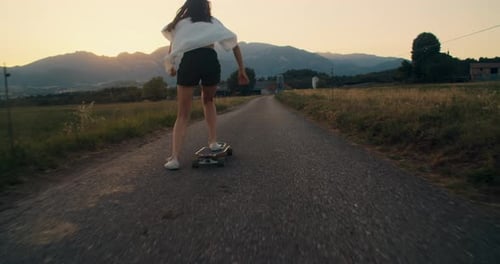Unrecognizable Woman Ride on Skate Longboard at Sunset with Mountain Landscape