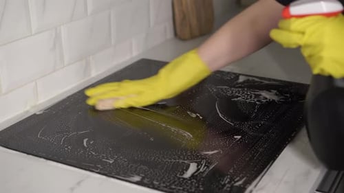Woman Cleans Black Glass Stovetop with Spray and Sponge
