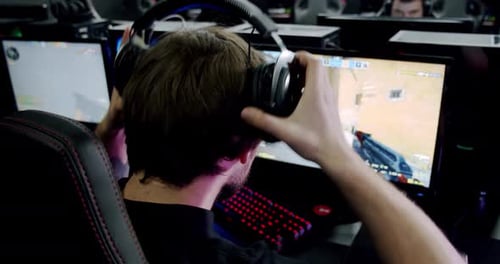 A Man Gamer Puts on Headphones with a Mic On and Starts Playing Online Video Game , Close Up