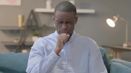 Man Coughing and Rubbing Chest Indoors on Couch