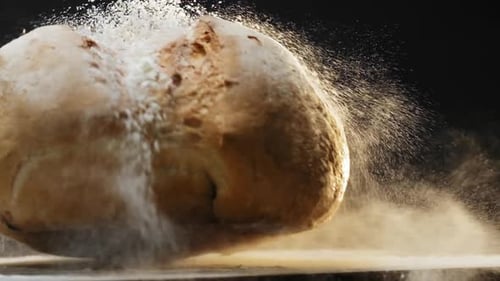 Wheat Bread Loaf with Flour Falls Down Onto Table on Black