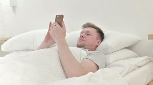 Man Relaxing in Bed Using Mobile Phone