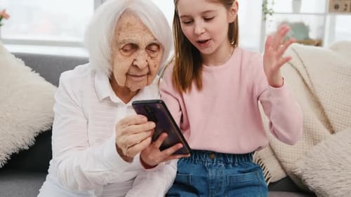 Grandmother and Granddaughter Looking at Phone Together on Sofa