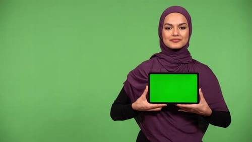 A Young Muslim Woman Shows a Tablet with Green Screen to the Camera with a Smile Green Screen