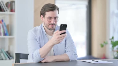 Attractive Man in Glasses Using Smartphone in Office