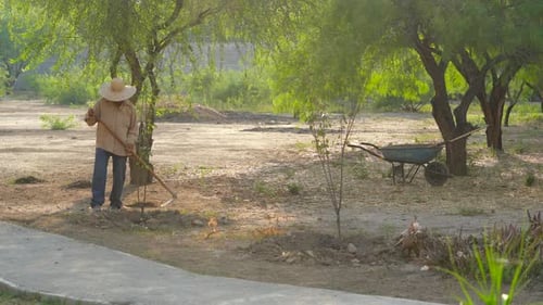 Unrecognizable Man With Hat Working In The Field And Large Garden With Worker Tool