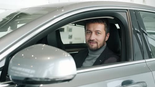 Smiling Man Sits Inside Modern Car in Showroom