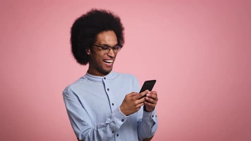 Man Using Phone Expressing Joy on Pink Background