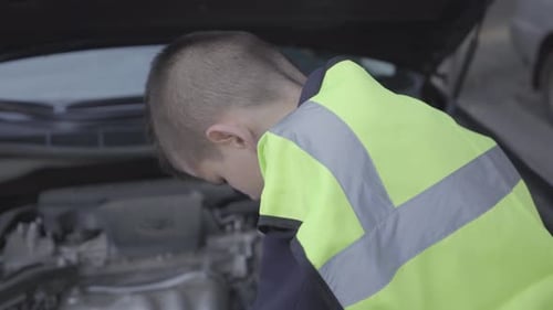 Confident Small Boy Wearing Safety Equipment Standing By the Open Hood of a Broken Car
