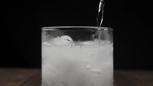 Clear Liquid Pouring into Glass Over Ice Cubes