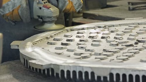 Verbergen Sie die Hände eines Arbeiters, der ein Metallgussteil mit einer Schleifmaschine poliert