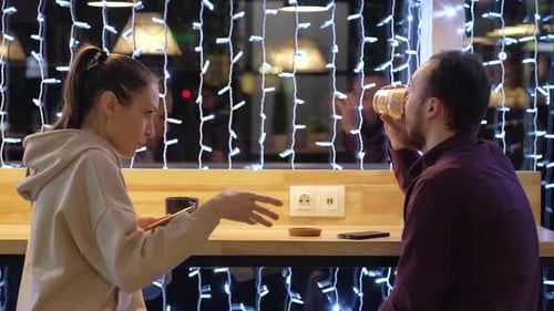 A couple sitting in a cafe, talking, drinks coffee and use smartphone.