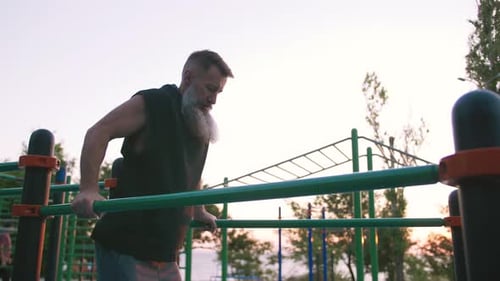Fit gutaussehender Mann mittleren Alters mit langem grauem Bart, der Liegestütze an Barren auf Sportplätzen macht