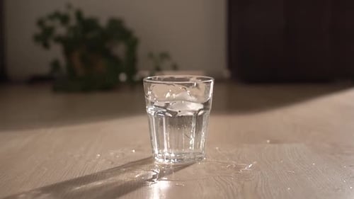 Ice Falls in a Glass of Water Slow Motion. Morning Light on the Floor Where a Transparent Glass