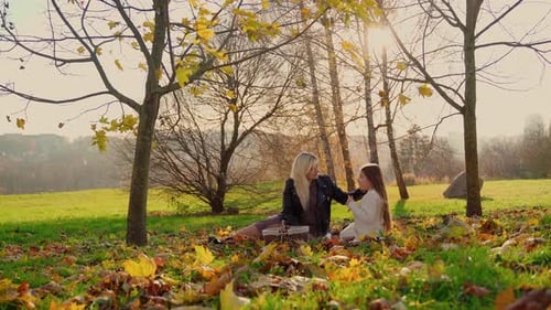 Mother and daughter have picnic at autumn park outdoors. Two females smile and laugh spending time