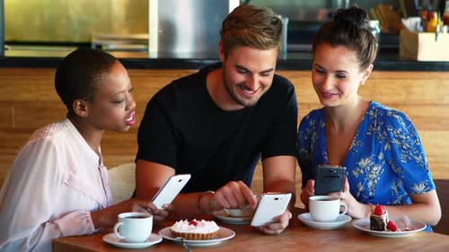 Friends Laughing and Using Smartphones in a Cafe