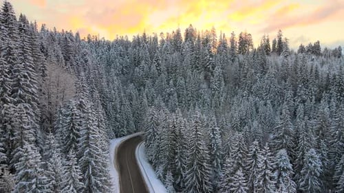 Aerial view of winter landscape with snow covered mountain hills and winding forest road in morning.
