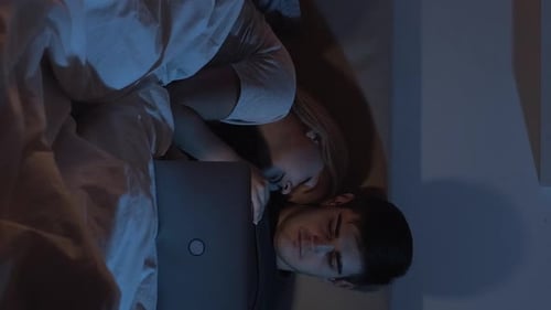 Couple Resting in Bed with Laptop at Night
