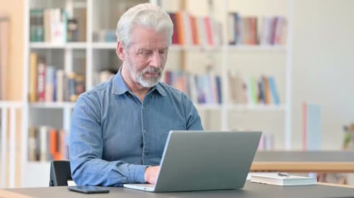 Mature Man Works on Laptop at Home Desk