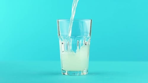 Fruit Fizzy Lemonade Soda Cold Beverage Drink Pooring Into Faceted Glass on Colored Blue