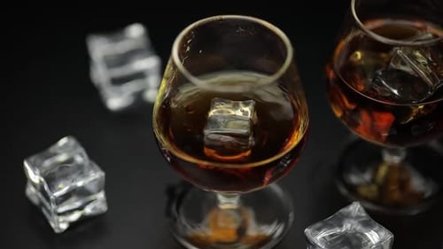 Ice Cube Dropped Into Glass of Alcohol Drink Whiskey, Cognac. Slow Motion