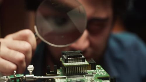 Engineer Inspecting Computer Circuit Board with Magnifying Glass