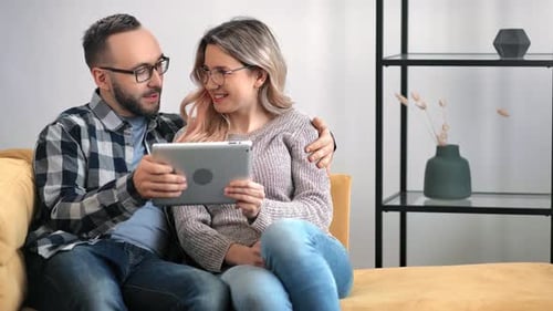 Couple Relaxing on Couch Looking at Tablet