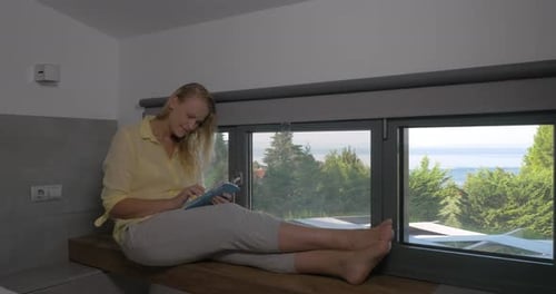 Woman Uses Tablet While Sitting by Window