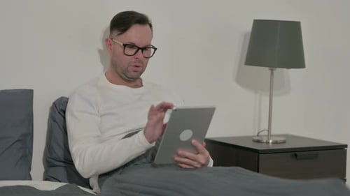Man with Glasses Sitting in Bed Using Tablet