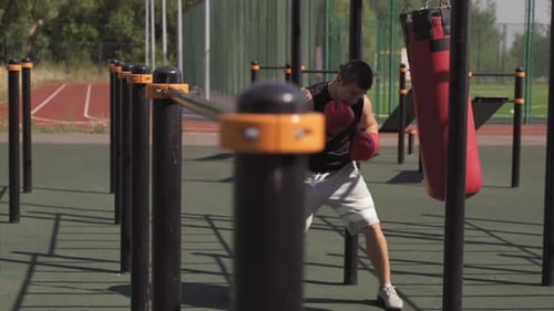 Young Man Boxing Heavy Bag in Outdoor Gym
