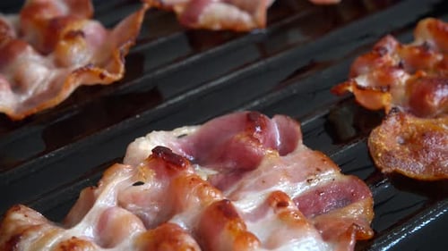 Fried bacon slices rotate in a grill pan.