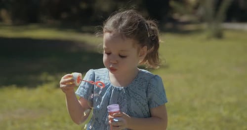 Cute Girl Blowing Bubbles in a Green Park