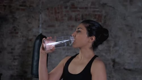 Beautiful Indian girl drinking water in sport gym. Female drinks water after exercise in gym