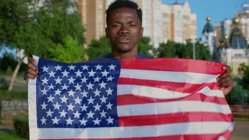 Man Holding American Flag Outdoors in Urban Setting