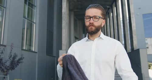 Man Places Jacket on Shoulder by Office Building