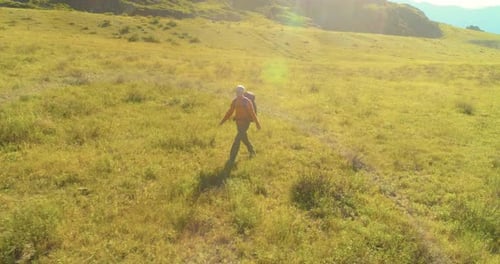Flight Over Backpack Hiking Tourist Walking Across Green Mountain Field. Huge Rural Valley at Summer