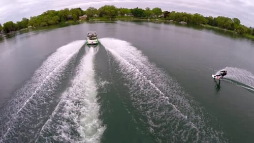 Aerial birds-eye drone view of a man wakeboarding behind a boat.