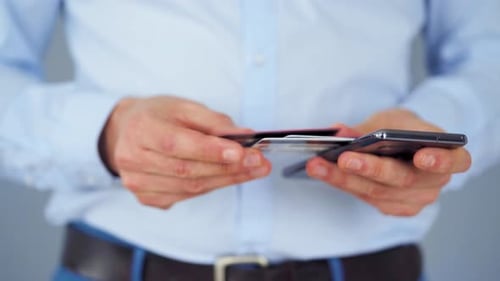 Formal gekleideter Mann wählt aus mehreren eine Kreditkarte aus und gibt ihre Nummer in ein Smartphone ein