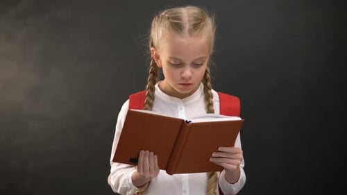 Young Girl Reads a Book Wearing Backpack