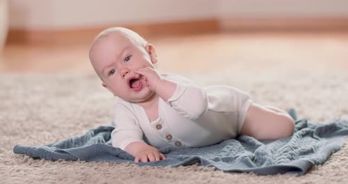 Close Up of Little Baby Crawling on the Rug and Blanket on the Floor Looking Upwards and Pushes Its
